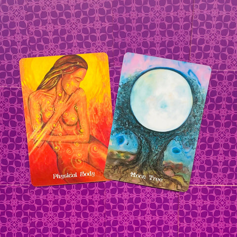 Oracle kortos: dvi iliustruotos kortos — oranžinė Physical Body ir mėlyna Moon Tree, padėtos ant violetinio raštuoto fono, rodomas poros kortų variantas