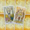 Tarot kortos su akvarelinėmis iliustracijomis — dvi atviros monetų kortos (Three/Four of Coins) prieš geltonas ornamentuotas nugarėles, skirtos komplekto parodymui