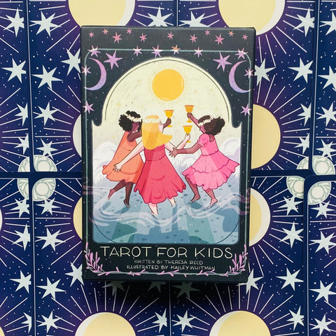 Tarot kortos vaikams dėžutėje su trijų mergaičių iliustracija ir karštai rožine, geltona bei tamsiai mėlyna žvaigždėta fone