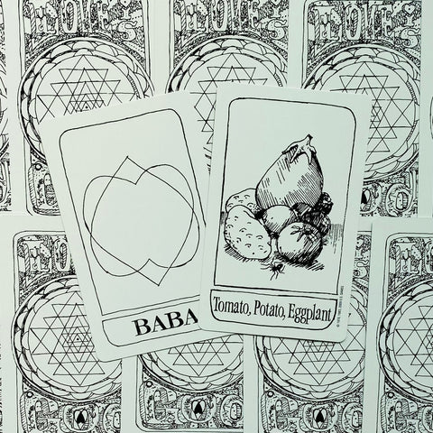 Tarot kortos su juodai baltu iliustracija: atverstoje kortoje tomatas, bulvė ir baklažanas, matomas kortų nugarėlių raštas