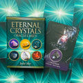 Oracle kortų rinkinys Eternal Crystals (Jade‑Sky) žalsvame dėkle, šalia atversta Obsidian korta nurodanti apsaugą ir šaknų čakrą