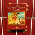 Prekės puslapis — raudonas The Lover's Path Tarot kortų dėklas, priekinis vaizdas su angelu ir gulinčia moterimi, autorius Kris Waldherr, centruotas ant raudono fono