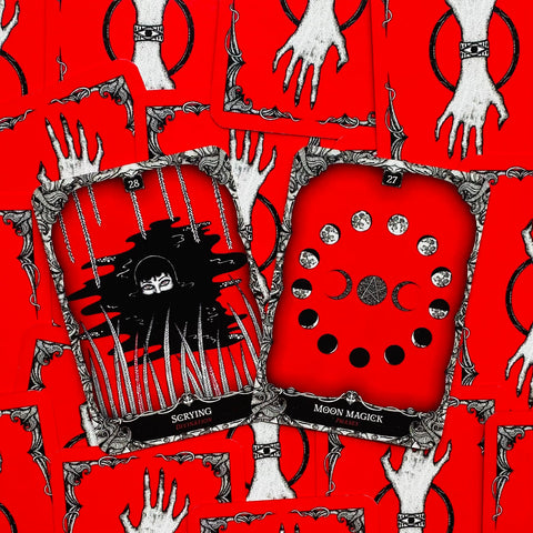 Tarot kortos raudonais nugarėliais, dvi atvertos kortos Scrying ir Moon Magick su juodai baltu ornamentu ir mėnulio fazėmis