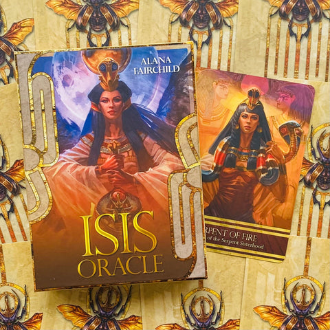 Isis Oracle kortos Alana Fairchild dėžutėje su auksuotais akcentais ir atversta viena korta šone, rodanti meno variantą