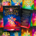 Galactic Symbols kortų rinkinys (Sharina Star), spalvota kosminė dėžutė su 50 būrimo kortų, viena korta atversta ir rodoma tekstu