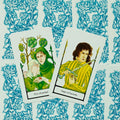 tarot kortos ant mėlyno gėlių dizaino fono, dvi kortos (Pentaklių penketukas ir Kardų puslapis) fotografuotos iš viršaus