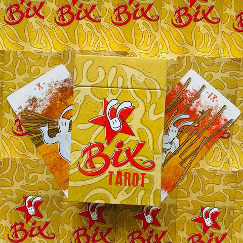 Bix Tarot kortų kaladė geltoname dėkle su raudonu logotipu, dvi ištrauktos kortos su oranžiniais raštais parodytos iš viršaus, prekės pakuotės vaizdas