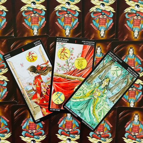 Tarot kortos su rytietiškais piešiniais — trys atverstos kortos ant raudonų nugarėlių fono, arti viršaus kampo perspektiva
