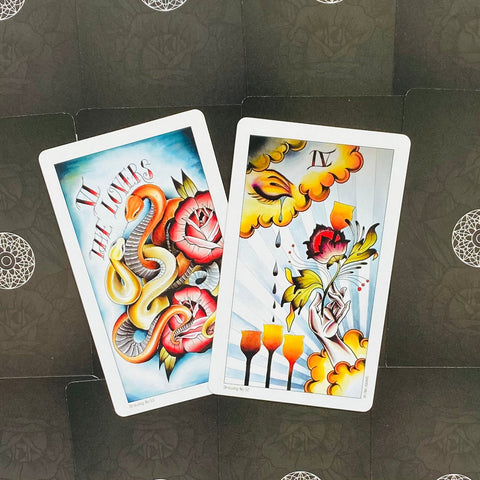 Tarot kortos su ryškiomis tatuiruočių iliustracijomis — "The Lovers" (gyvatė ir rožės) ir keturi taurės ant tamsaus raštuoto fono, šiek tiek pakreiptos