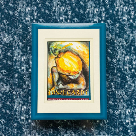 Rėmas su Soulcards atspaudu, tamsiai mėlynas išorinis rėmas ir kreminis matas, centre pakabintas prieš mėlyną raštuotą sieną