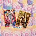Tarot kortos – dvi atviros angelų kortos (Rikbiel ir Ariel) ant pastelinio rožinio–melsvo nugarėlių fono, kolekcijos dizaino variantas