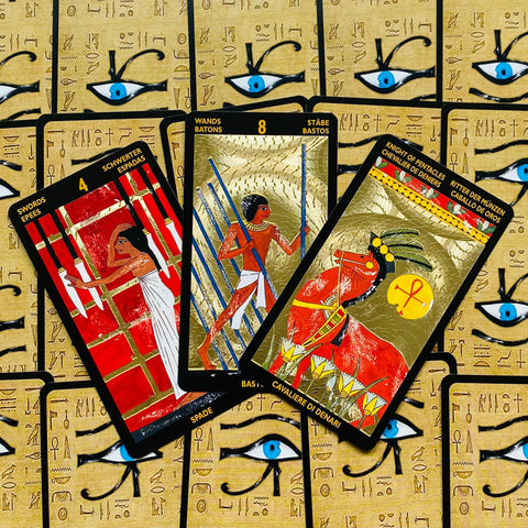 Tarot kortos Egypto dizaino, trys atverstos kortos su auksinėmis detalėmis ir mėlynais akių simboliais, rodomos iš arti