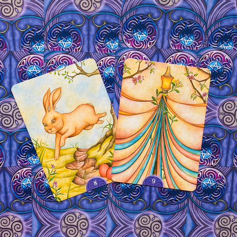 Tarot kortos dvi iliustruotos kortos: bėgantis triušis ir kaspinų stiebas, šiltos pastelinės spalvos ir ornamentinis violetinis fonas