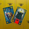 Symbolon tarot kortos: dvi atverstos kortos su spalvingomis priekinėmis iliustracijomis ant geltono dėklo, matomi aukso apvadai ir skirtingi kampai