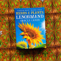 Lenormand kortos su geltonu saulėgrąžos piešiniu ant mėlynos dėžutės, tiesiai iš priekio, ant raštuoto fono