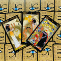 Tarot kortos egiptietišku dizainu su aukso folija, trijų kortų išdėstymas (Karalienė monetų, 3 monetos, 7 taurių) ant fono su Horuso akimis