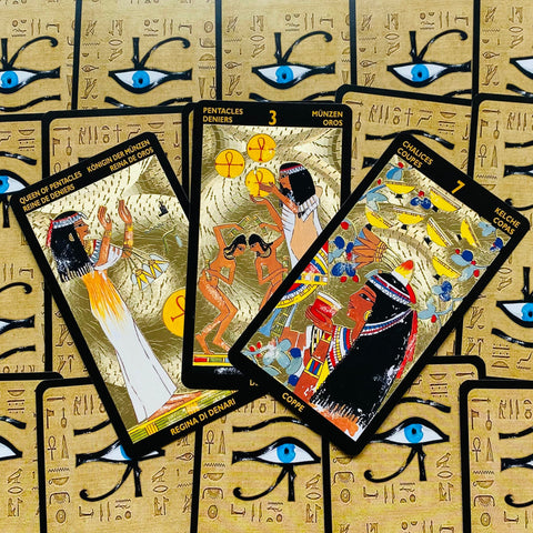 Tarot kortos egiptietišku dizainu su aukso folija, trijų kortų išdėstymas (Karalienė monetų, 3 monetos, 7 taurių) ant fono su Horuso akimis