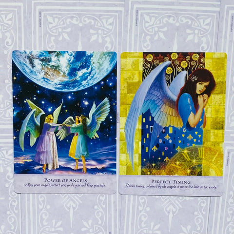 angelų kortos: dvi atverstos kortos — „Power of Angels“ su mėlyna naktine scena ir „Perfect Timing“ su auksiniu fonu, horizontalus kampas, skirtingos iliustracijos