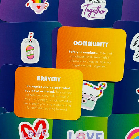 Įkvepiančios kortelės rinkinys – arti sufokusuotos oranžinės „Community“ ir „Bravery“ kortelės su vaivorykštės lipdukais, aiškiai matomas tekstas ir dizainas