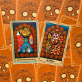Tarot kortos oranžiniais kaukės nugarėliais, dvi atverstos kortos Cuatro Elementos ir Comida su ryškiomis iliustracijomis