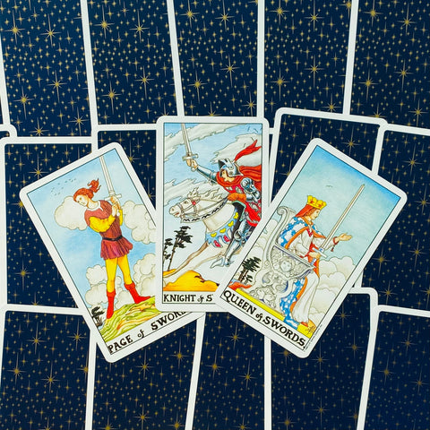 Tarot kortos Rider–Waite stiliaus, trys kardų rūmų kortos (Page, Knight, Queen) priekiniu kampu ant tamsios žvaigždėtos nugarėlės