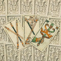 Tarot kortos rankų darbo itališkos versijos trijų kortų išdėstymas su spalvotais lazdų ir kardų motyvais ir ornamentuotu nugarėlių fonu