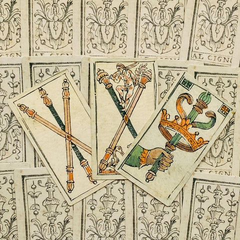 Tarot kortos rankų darbo itališkos versijos trijų kortų išdėstymas su spalvotais lazdų ir kardų motyvais ir ornamentuotu nugarėlių fonu