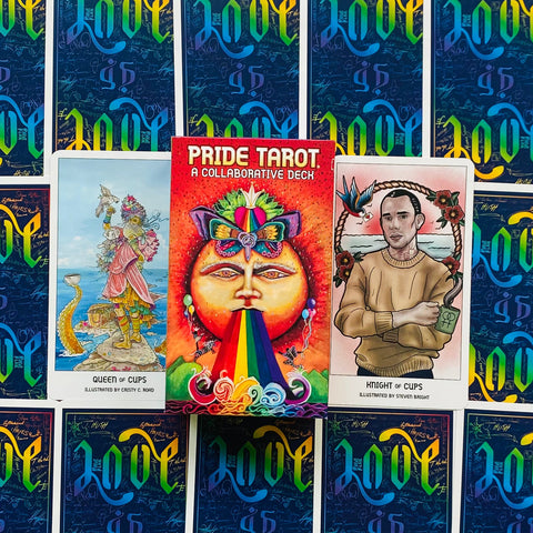 Pride Tarot kortų rinkinys su ryškia vaivorykšte dėkle, pažymėtas uždaru deniu ir atidengtomis Queen of Cups ir Knight of Cups kortomis