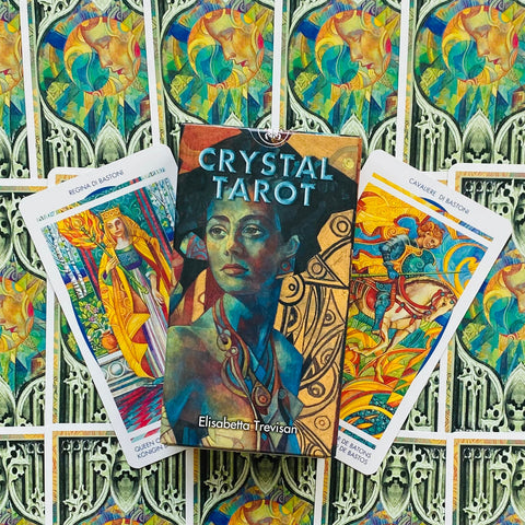 Crystal Tarot kortų dėžutė su Elisabetta Trevisan viršeliu, trys atvertos ryškios kortos ir ornamentinis fonas uždengtas kortomis