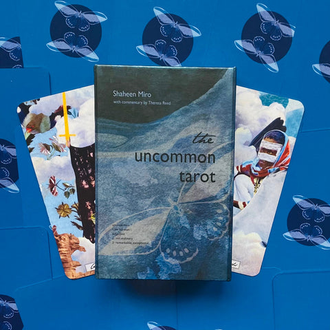 tarot kortos Uncommon Tarot mėlyname dėkle, matomas dėklo viršus ir dvi atviros iliustruotos kortos ant mėlyno fono