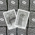 Tarot kortos juoda‑balta kolekcija, dvi atvertos kortos (Sinmara ir Eimyrja) ant raštuotų nugarėlių fono