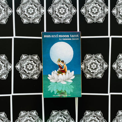 Sun and Moon tarot kortos dėžutė (Vanessa Decort) centre ant ornamentuotos juodos kortų išklotinės, mėlynas viršus su lotoso motyvu