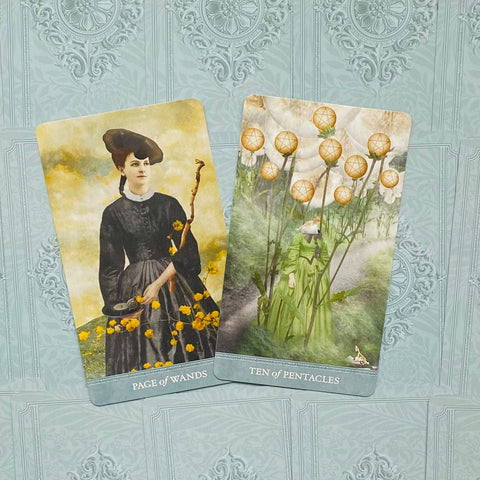 Tarot kortos dviejų pavyzdžių komplektas: Page of Wands ir Ten of Pentacles ant šviesiai mėlyno ornamentuoto fono