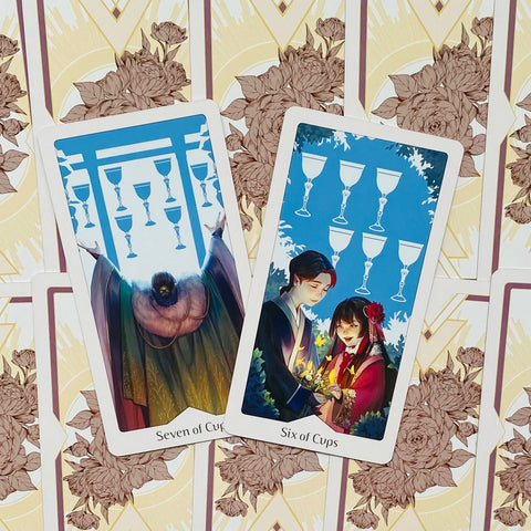 Tarot kortos su atversta Six of Cups ir Seven of Cups — mėlyni iliustracijos tonai ir dekoratyvios gėlių nugarėlės