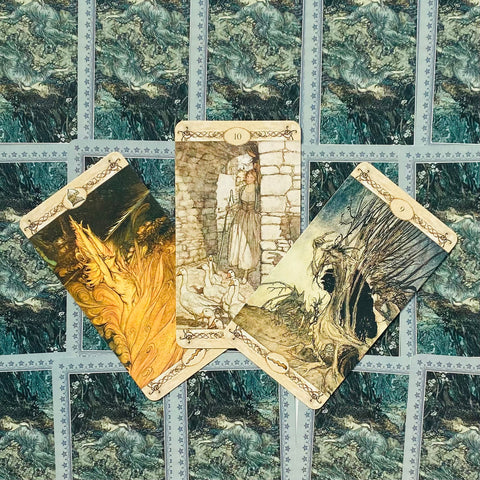 tarot kortos atverstos trimis kortomis: centre 10 su žąsimis, kairėje ugninė scena, dešinėje medinė kaukė, matyti mėlyni nugarėlių raštai