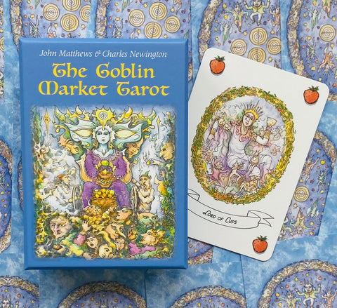 Taro kortų rinkinys Goblin Market mėlyname dėkle, iš šono matoma atversta Lord of Cups korta su braškėmis kampuose