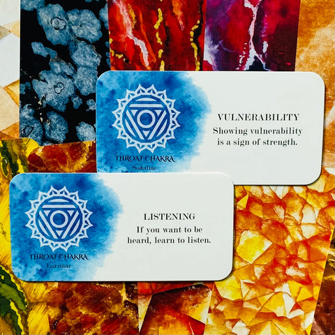 Čakros kortos: dvi mėlynos gerklės čakros kortelės (Sodalite, Larimar) su tekstais „Vulnerability“ ir „Listening“ ant spalvoto akmenų fono