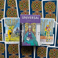 Tarot kortos Universal — violetinė dėžutė pristatoma su mėlynomis auksinėmis kortų nugarėlėmis ir keliomis atvertomis kortomis
