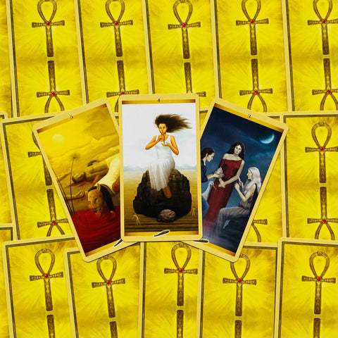 Tarot kortos geltonomis nugarėlėmis, trijų kortų išklotinė centre: vidurinė korta stačia su moterimi baltame rūbe