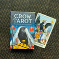 Crow Tarot kortų rinkinys dėžutė mėlyna su varnos iliustracija, šalia atversta Pentacles korta ant tamsaus raštuoto fono