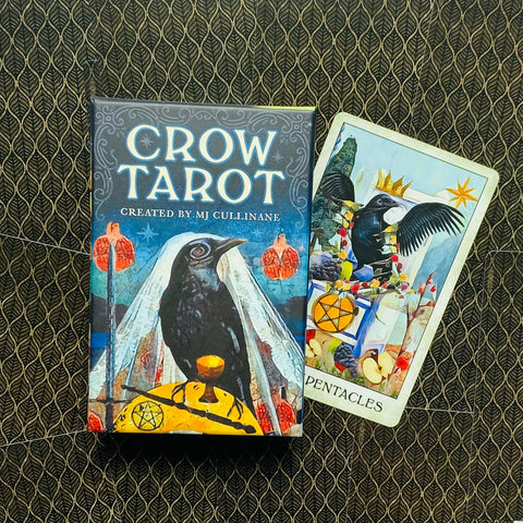 Crow Tarot kortų rinkinys dėžutė mėlyna su varnos iliustracija, šalia atversta Pentacles korta ant tamsaus raštuoto fono