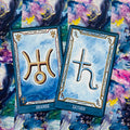 Tarot kortos su mėlynomis kraštinėmis ir auksiniais Uraną bei Saturną žyminčiais simboliais ant akvarelinio kosminio fono, porinis variantas