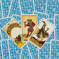 Tarot kortos Rider‑Waite stiliaus su mėlynomis nugarėlėmis, trys atvertos Taurių kortos (X, Puslapis, Riteris) centre
