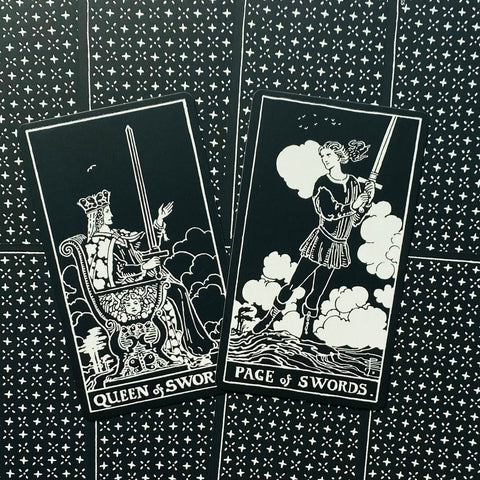 Tarot kortos 78 dalių rinkinio juodai baltos Rider‑Waite stiliaus, plokščiai išdėstytos; matomos Queen of Swords ir Page of Swords kortos