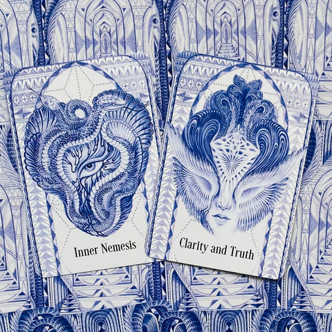 Orakulų kortos atverstos dviem: mėlynos ornamentinės kortos su veidų motyvais, matomos „Inner Nemesis“ ir „Clarity and Truth“ kortos, artimas planas