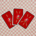 tarot kortos su ryškiai raudonomis nugarėlėmis, trijų kortų vėduoklės išdėstymas ant rožinio raštuoto fono