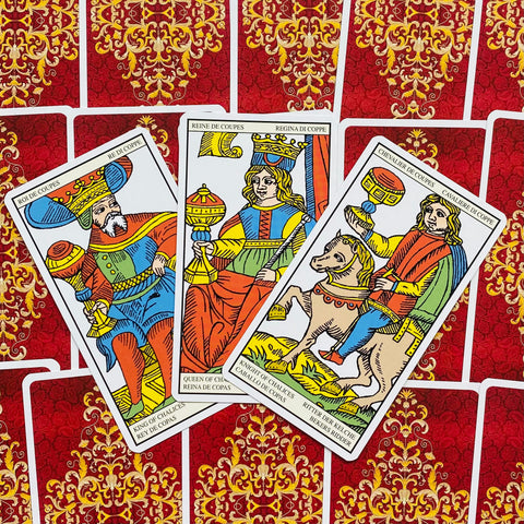 Tarot kortos Marseilio stiliaus – trys atverstos taurų rūšies figūros (karalius, karalienė, raitelis) ant raudonų ornamentuotų nugarėlių, kampu išdėstytos