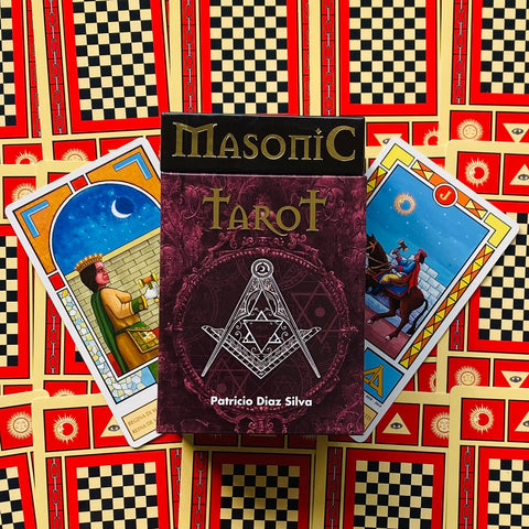 Masoniškas tarot rinkinys su bordo dėkle, dviem pavyzdiniais kortomis ir ryškia raudono‑geltono langų fono kompozicija