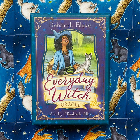 Orakulų kortos Everyday Witch — violetinė dėžutė su Elisabeth Alba iliustracija ant mėlyno, katėmis marginto fono