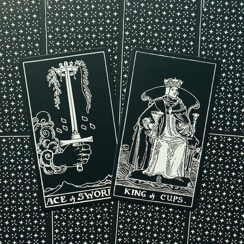Tarot kortos juodai baltos, dvi kortos (Ace of Swords, King of Cups) išdėstytos į šoną ant žvaigždėto fono